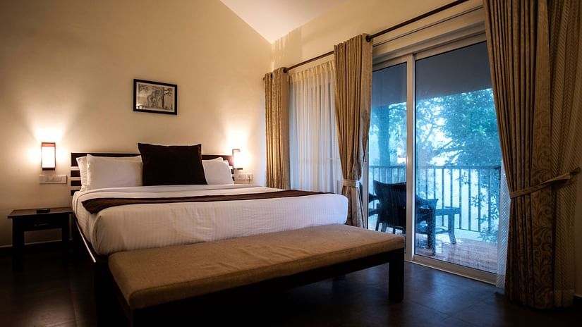 A bedroom features a bed, curtains on a glass door, and a view of the outdoors. - Abad Brookside Lakkidi, Wayanad