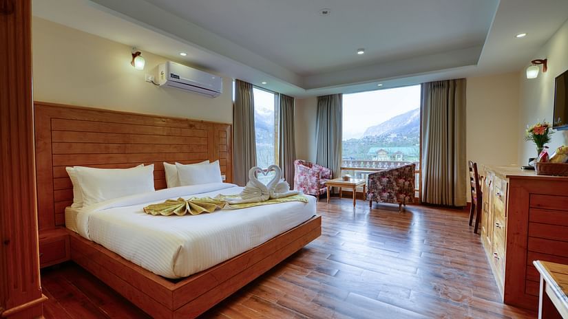 Premium Room at Clarks Inn Suites, Manali featuring a plush bed on well-furnished floor and a sitting space next to huge windows
