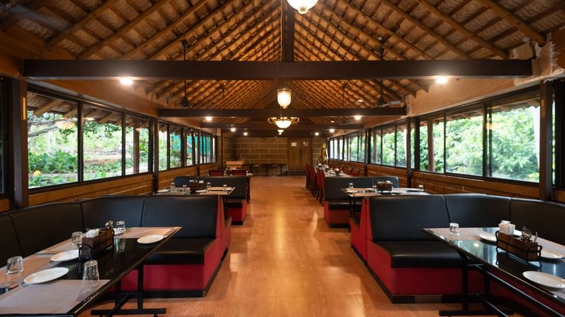 Aqua Restaurant at Ibex River Resort, Pollachi under ambient lighting with sloped thatched roof and wooden flooring with booths next to the windows