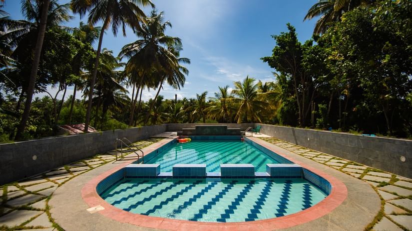 Swimming pool with crystal clear water and trees in the surrounding on a sunny day at Ibex River Resort, Pollachi