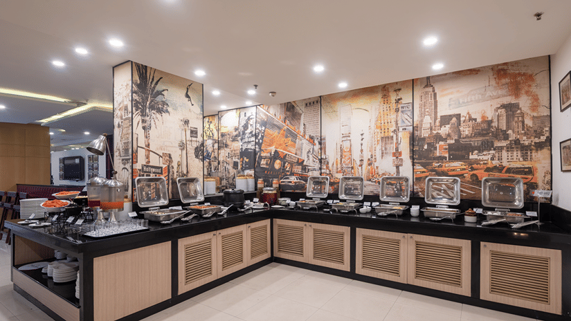 Buffet counter with serving dishes and a decorative mural in the corner at Mango Grove Hotel, Chandigarh.