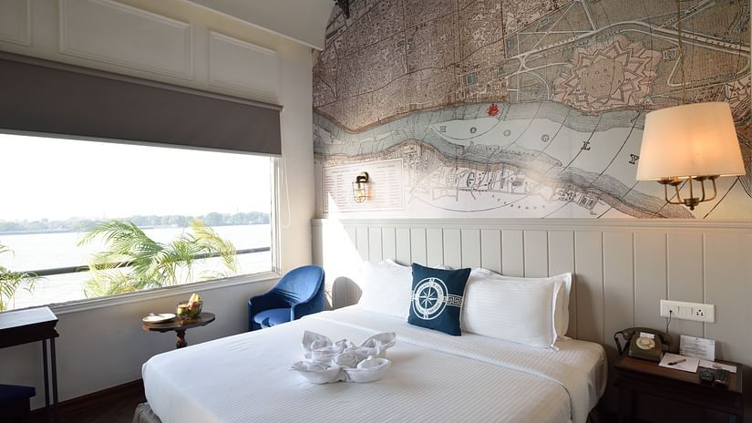 a well made bed with blue pillows and a lamp hanging above the bed - polo floatel kolkata