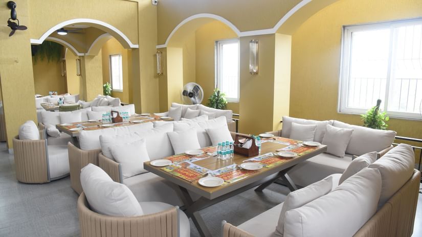 Outdoor dining space with beige sofas, wooden tables, and natural light at Pride Elite Raipur.