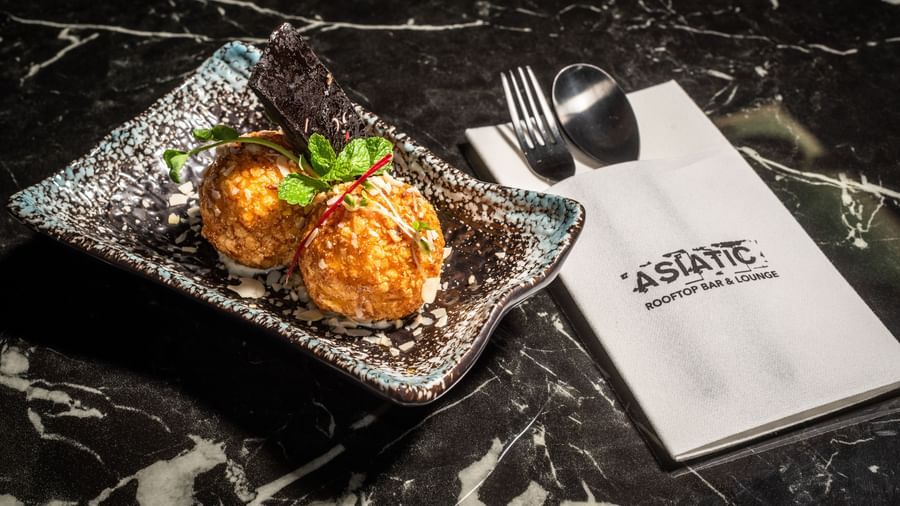 Plate of fried ice cream served at Asiatic Lounge, featuring a crispy golden coating over ice cream scoops, garnished and presented with the lounge’s branded napkin and cutlery on a marble table.