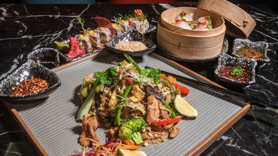 Mixed platter of Asian delicacies, including vegetables, noodles, and dim sum, served at Asiatic Lounge with sauces on the side.