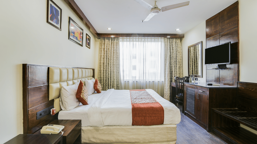 A neat, modern room, with a double bed, a flatscreen television, a small table beside the bed and a window with curtains - Hotel Bluestone Prime (Nehru Place), New Delhi