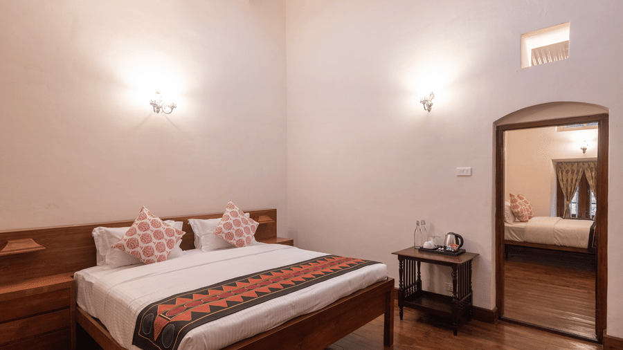 The warmly lit Mayfair Suite at Ibex Resorts, Coonoor (Leewood), with a large bed, bespreads, pillows, and a mirror..