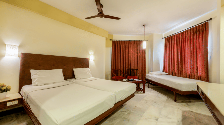 Spacious Deluxe Room at Jayaram Hotel, Pondicherry with a double bed, seating area, work desk and large windows.
