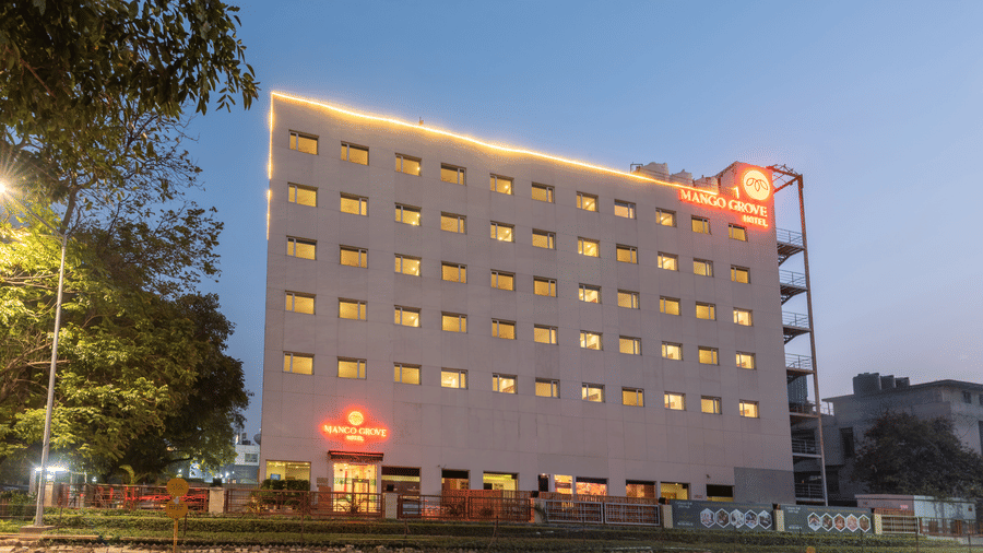 Exterior view of Mango Grove Hotel at dusk, beautifully lit with warm lights against a clear sky.