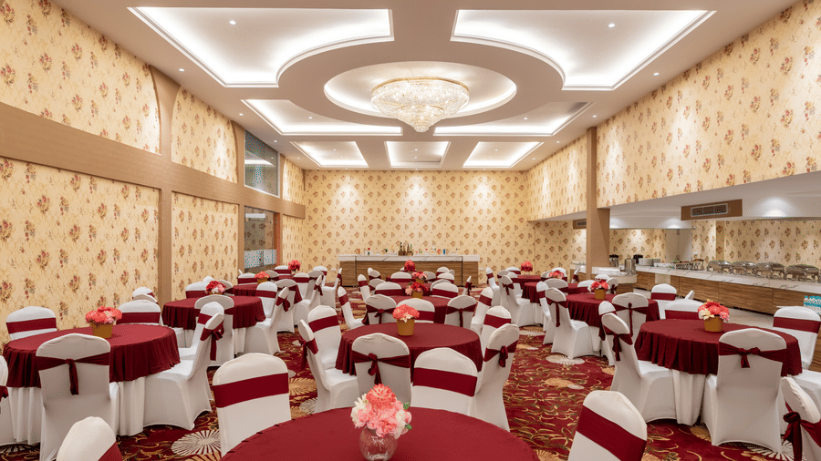 Banquet hall with round tables and an ornate ceiling chandelier at Mango Grove Hotel.