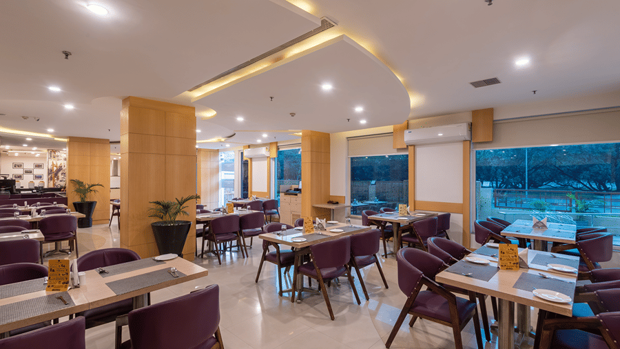 Restaurant seating area with tables, chairs and large windows bringing in daylight at Mango Grove Hotel.