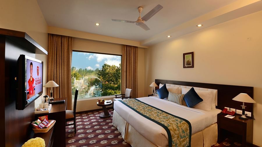 Executive Rooms in Moradabad featuring a plush bed next to a large window with picturesque view and a TV mounted on the wall in front of the bed