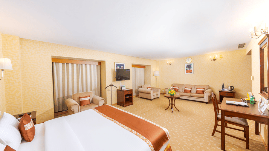 A room with a large bed, spreads, pillows, a window, a sofa set, and chairs. | MGM Mark Whitefield