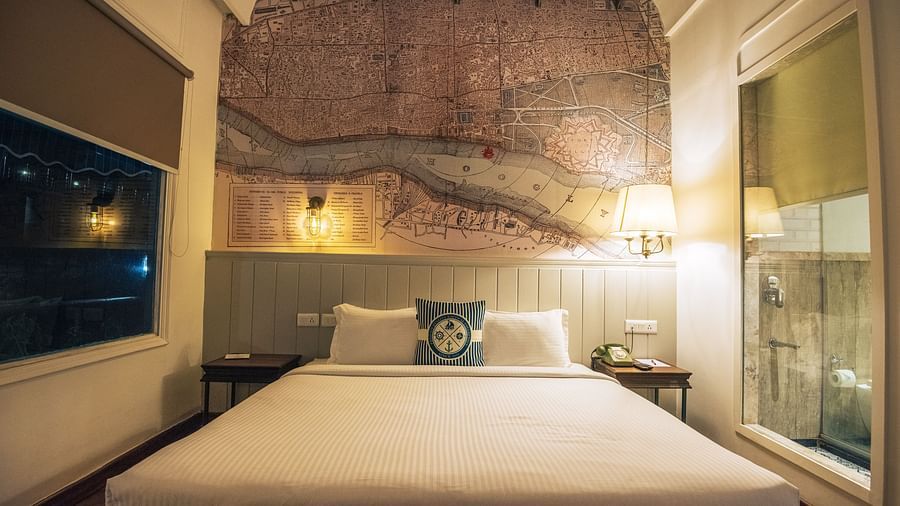 Interior of a bedroom with a large wall map, a queen-sized bed with striped bedding, and a compass-design cushion.