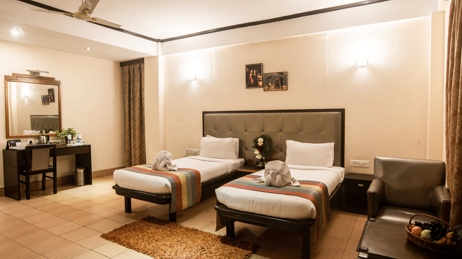 Room with twin beds, a fan, a chair, and tables at Polo Hotels, Tura.