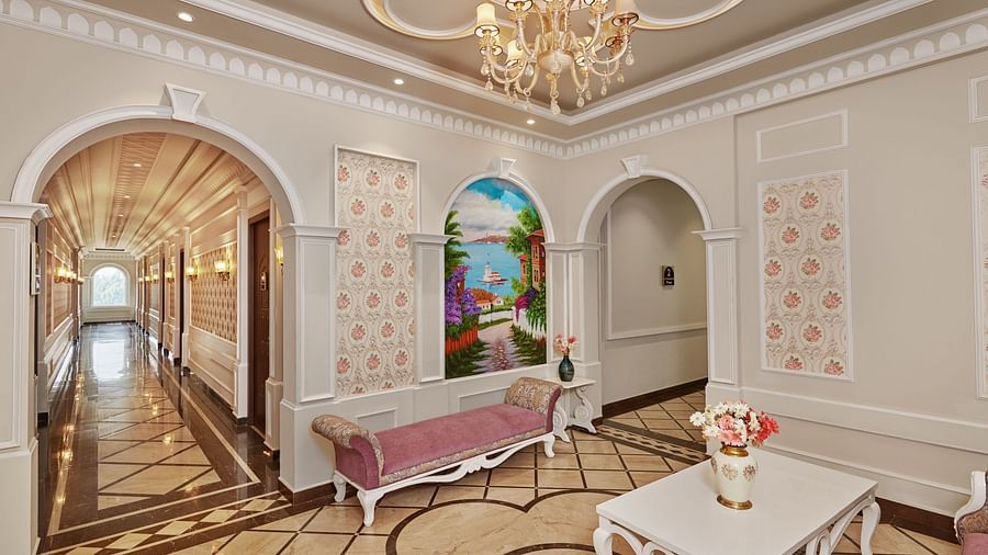 a divan, coffee tables with flower vases on them, a painting, and a chandelier in the corridor - Royal Kingdom Sarovar Portico, Pilibhit