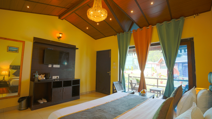 A large bed with many pillows and cushions, placed to face a flat screen TV, a tall mirror on a room with a chandelier | Sol Glow Resort, Nainital