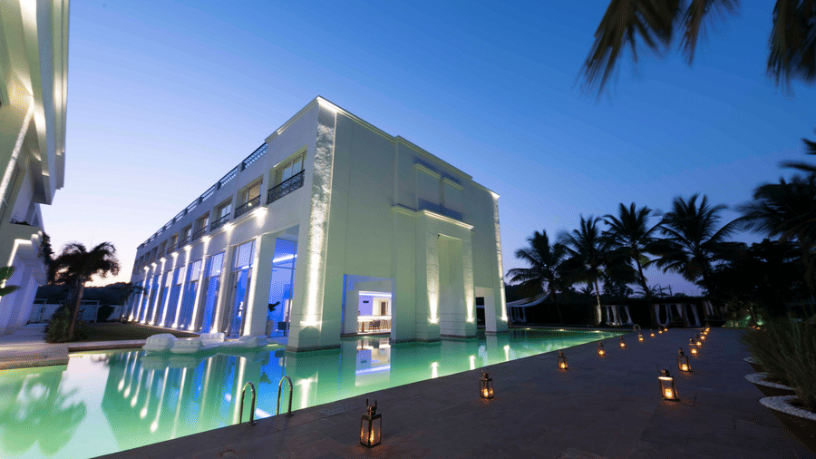  The Mansion House resort exterior at twilight with modern white columns, reflective pool, palm trees, lanterns, and blue-lit windows, creating a serene and luxurious evening atmosphere.
