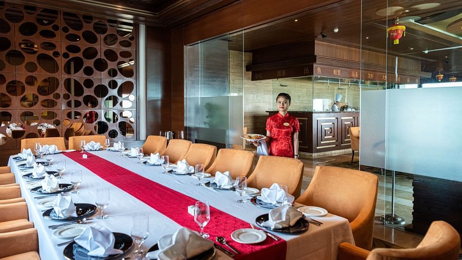 An image of a lady entering a dining area with one huge centre table and several chairs are placed around it - The Suryaa New Delhi