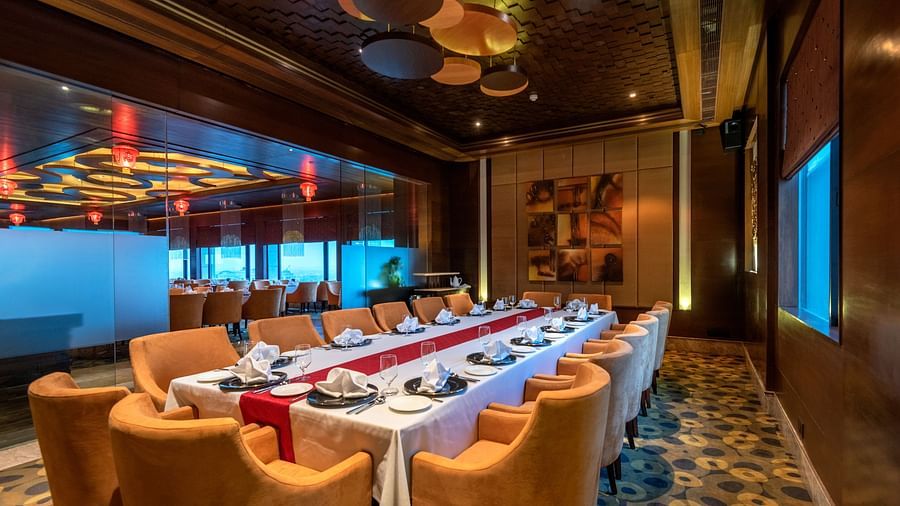 An image of a dining area with one huge centre table and several chairs are placed around it - The Suryaa New Delhi