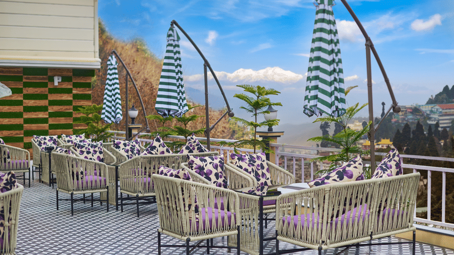 An outdoor deck with wicker seating and blue-and-white striped umbrellas under a blue sky | Voyage Rodhi Resort