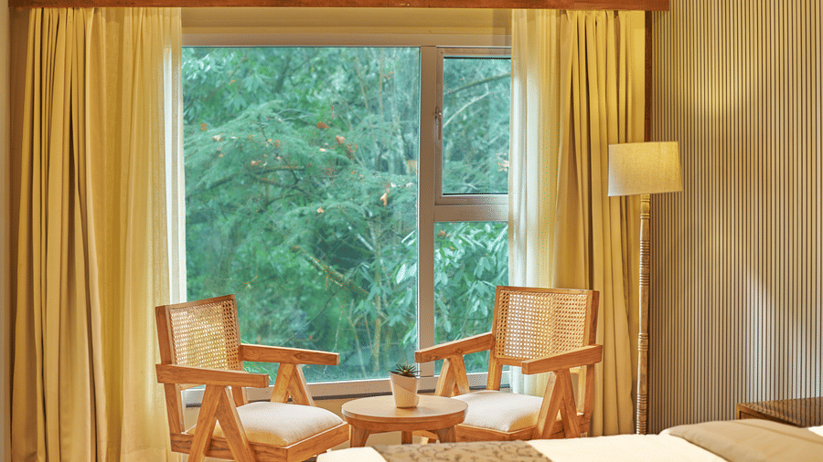 A sunny seating nook with 2 chairs, a round table, and a large window overlooking lush greenery | Voyage Rodhi Resort