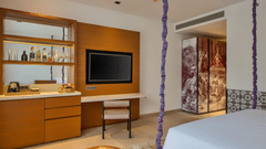 Deluxe Patio King Room featuring a plush bed facing the TV mounted on the wall and a work desk next to it with a minibar