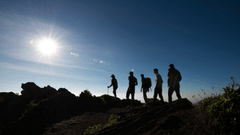 A view of a group of people's silhouette walking on a mountainous road with the sun above them. The Serai provides numerous Kabini packages including hiking.