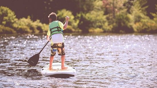 The image shows a boy paddle boarding on a lake.