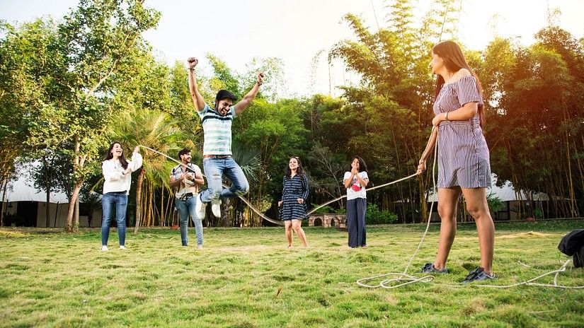 A group of adults and children playing tug of war in a grassy outdoor area, displaying joy and family bonding during a playful and competitive moment.