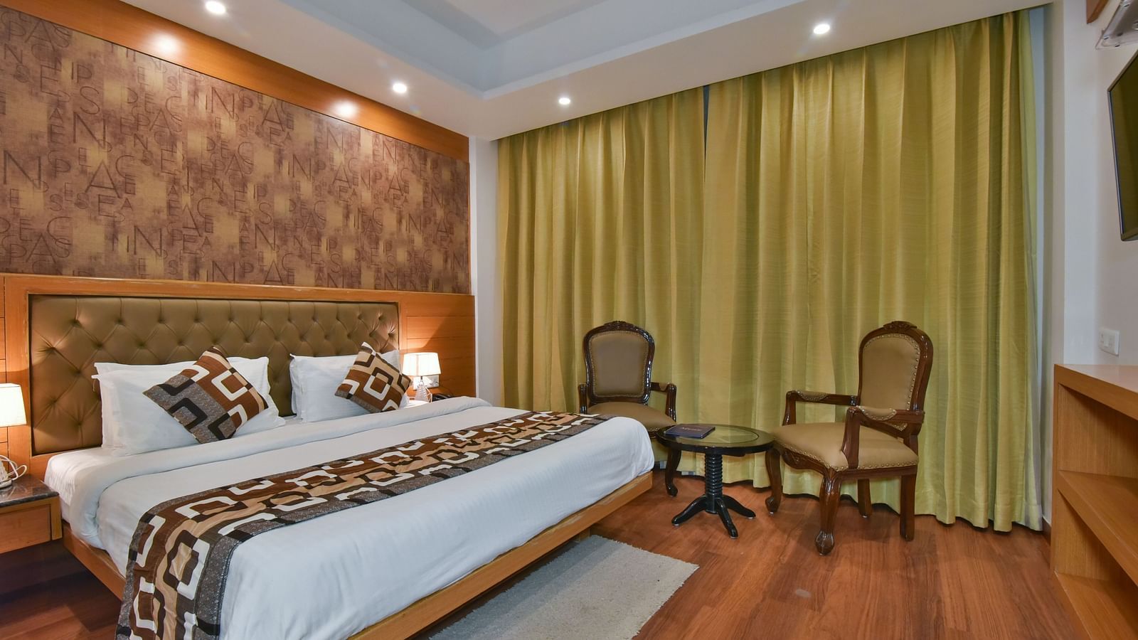 A large bed placed next to two chairs in the Deluxe Room at DLS Highland Resort and Spa, Mussoorie.