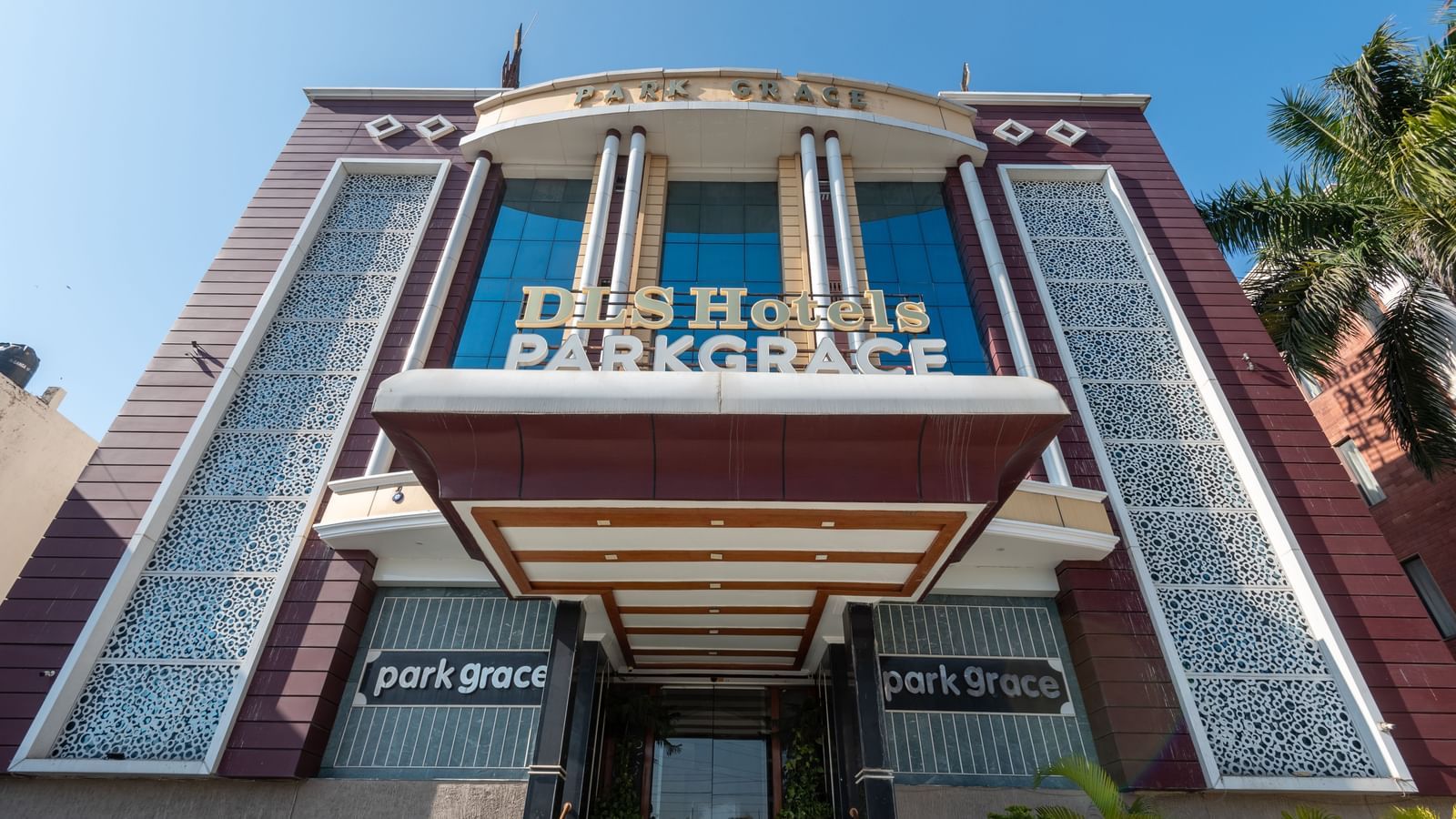 Exterior view from below of DLS Park Grace, Haridwar featuring a tall building, beautiful trees, and clear blue sky.
