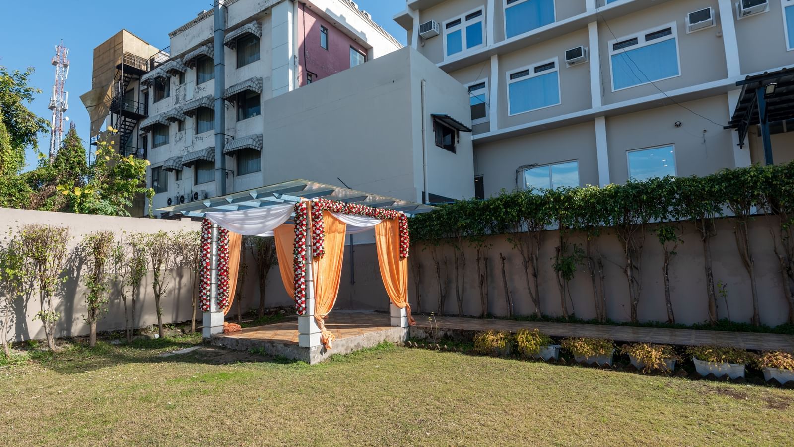An overview of the lawn area at DLS Park Grace, Haridwar featuring a ground and at one corner there is a bamboo pillar kind of structure decorated with fabrics and flowers.
