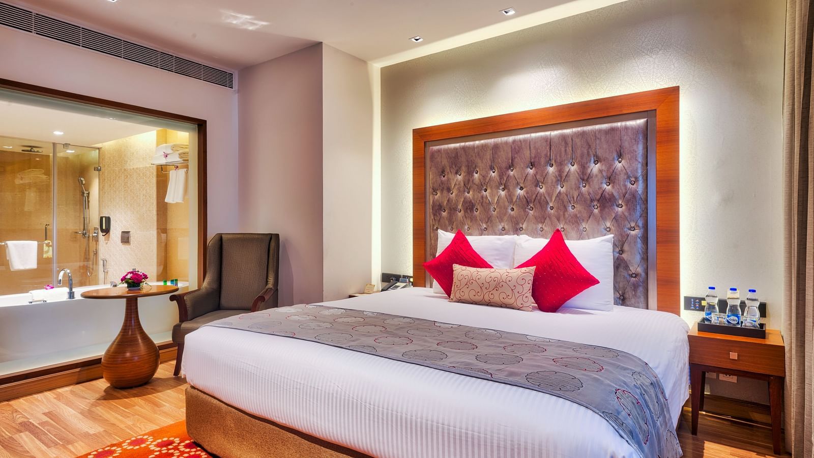 Deluxe Suite with king size bed, chair, side table and vase at Grand Chennai By GRT Hotels.