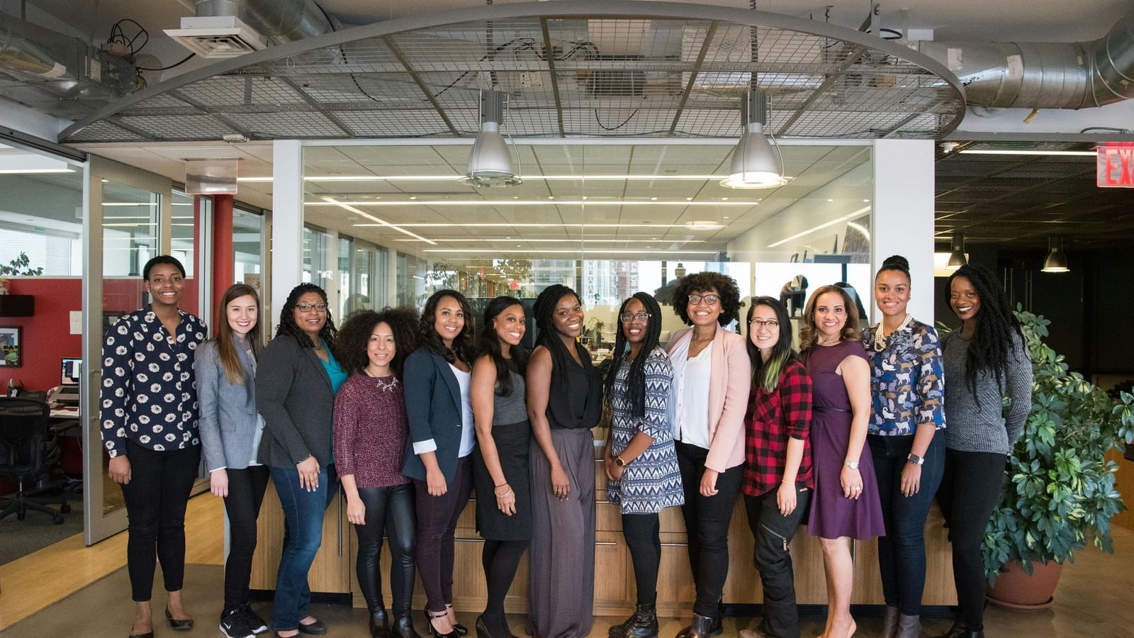 A group of diverse women and men standing together in a modern office space.