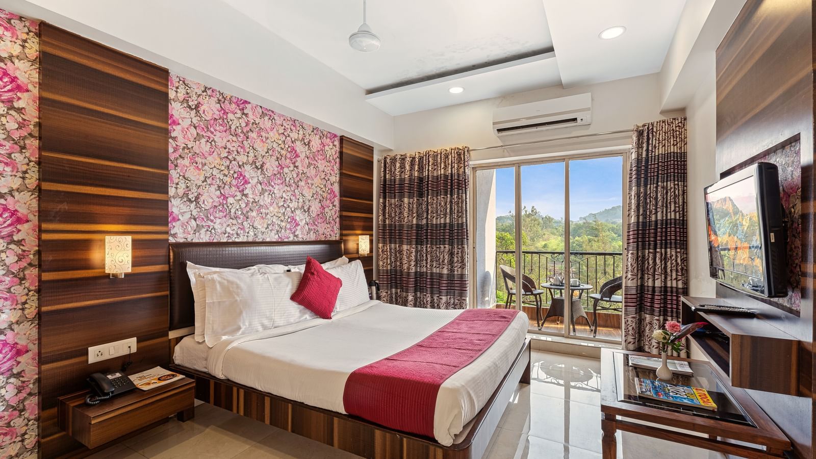 Charming guest room at Mayur Retreat featuring floral wallpaper, pink accents, a balcony, and a TV setup.
