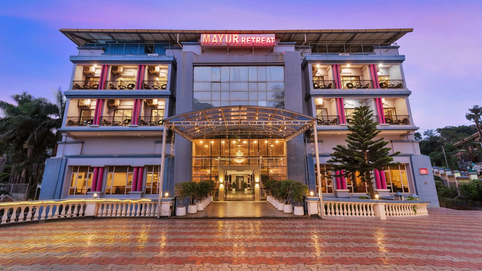 Front view of Mayur Retreat, a modern multi-storey hotel with illuminated glass entrance and symmetrical architecture.