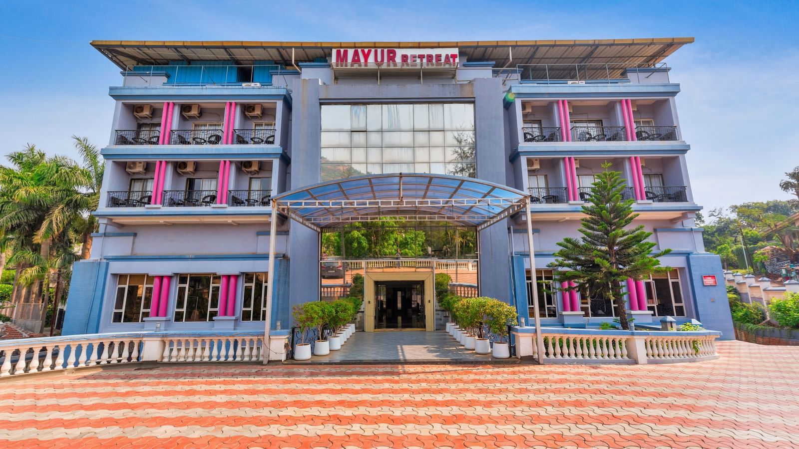 Facade of Mayur Retreat featuring multi-storied building surrounded by trees under a clear sky.