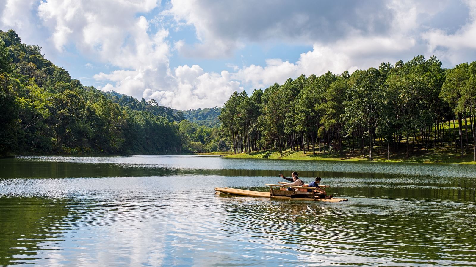 A serene view of Pookode Lake with a small boat floating on calm waters, surrounded by lush greenery and a clear sky.