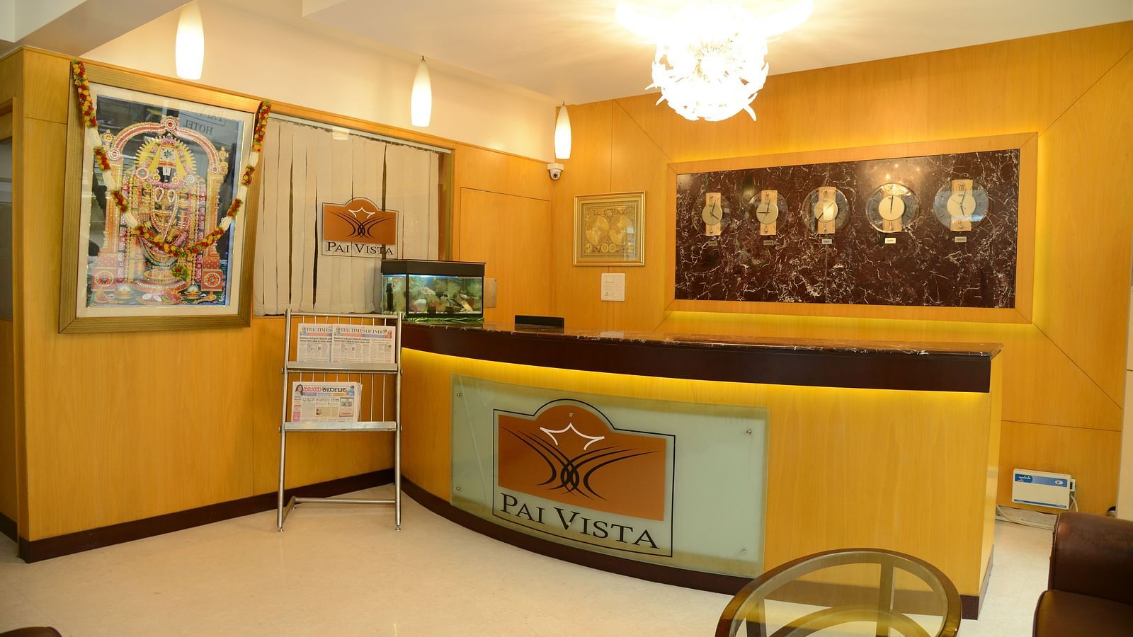 An image of a lobby featuring a reception desk, an aquarium,  a sofa and centre table, and  few wall clocks fixed on the wall beyond the desk - Pai Vista KR Road Luxury Hotel Bangalore