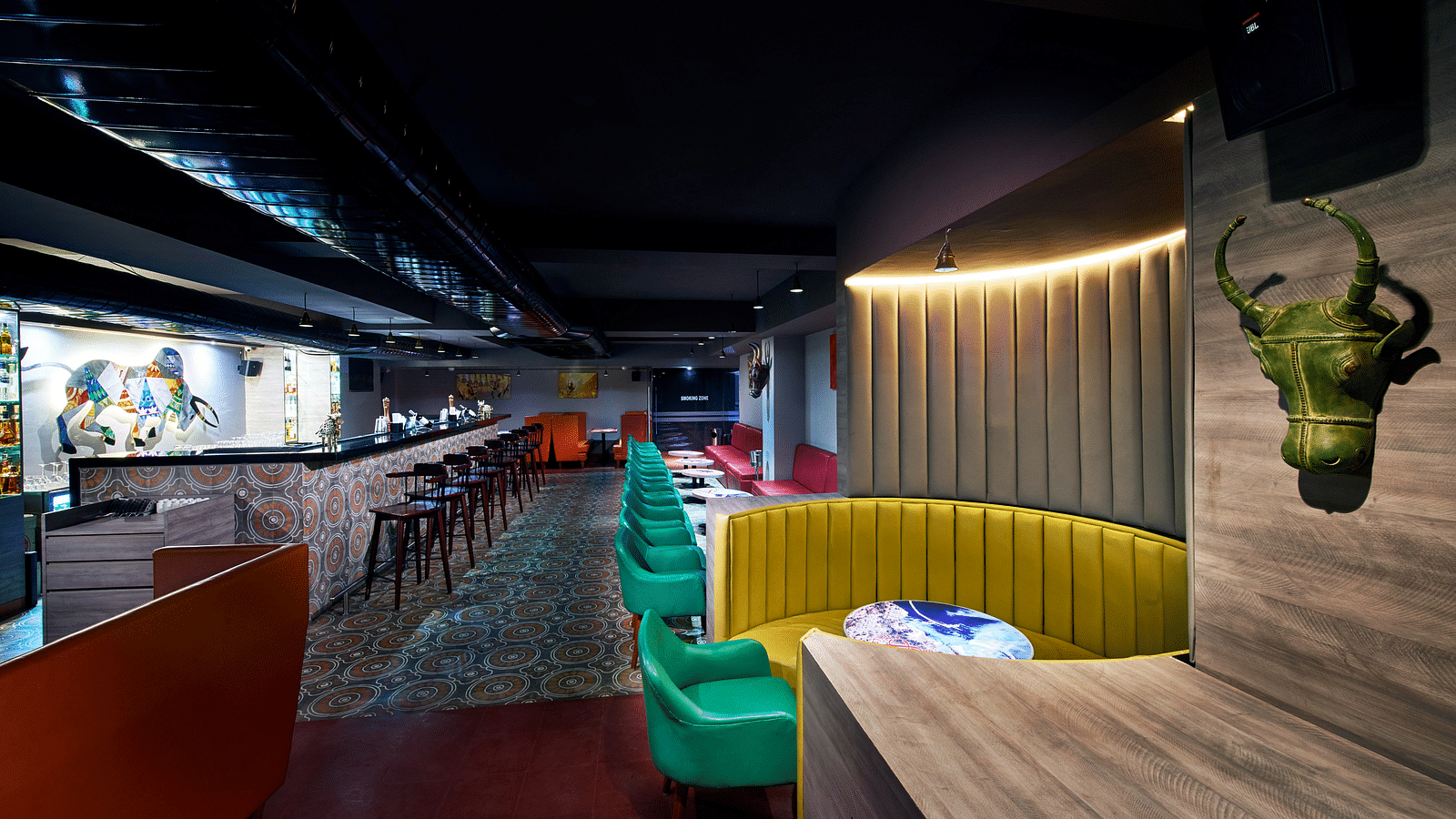 A brightly lit bar with red couches, a long bar counter, and a colorful wall mural | Regency Tirunelveli By GRT Hotels
