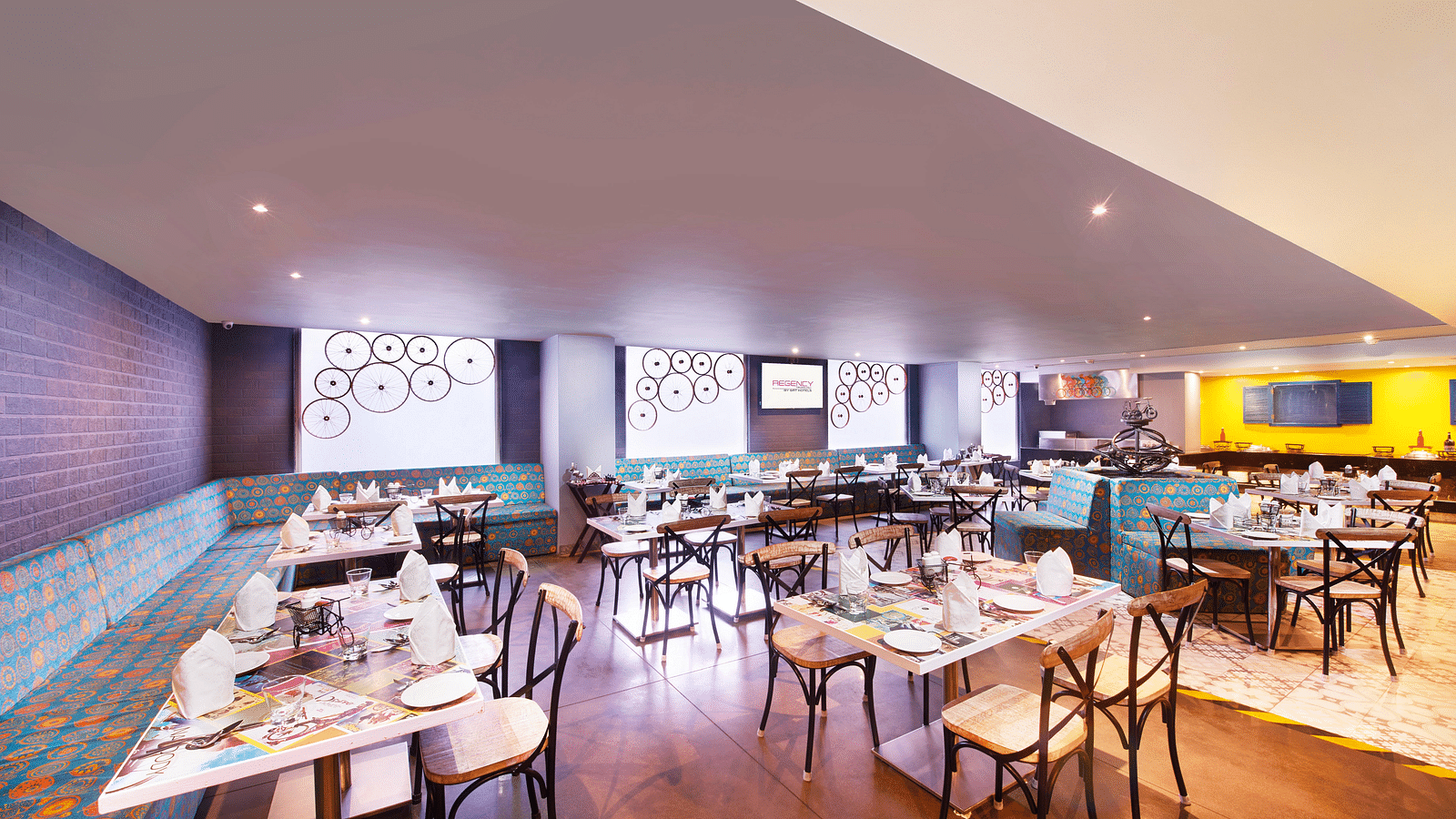 A brightly lit restaurant with chairs, a long bar counter, and a colorful wall mural | Regency Tirunelveli By GRT Hotels