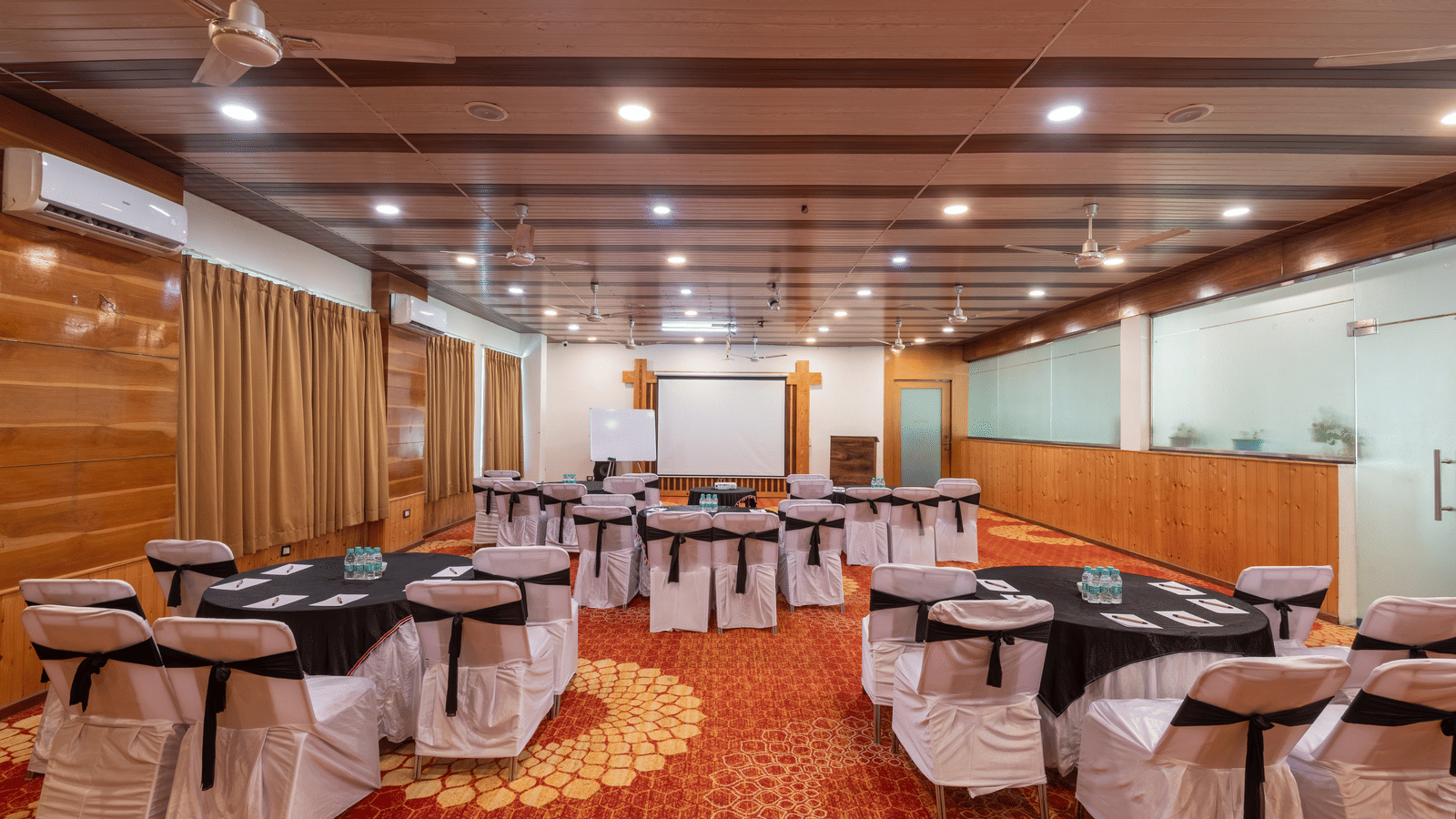 Bright banquet hall with tables and chairs om decorative orange rug at DLS Hotels On The Ganges.