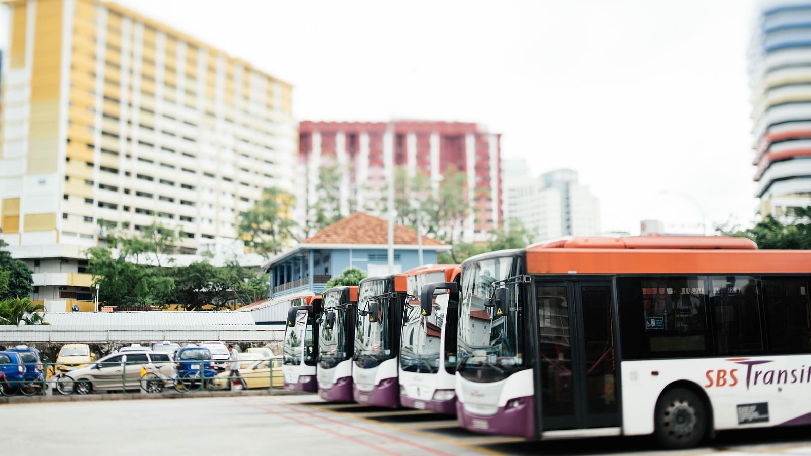 Busses parked in the bus depot with building in the background.