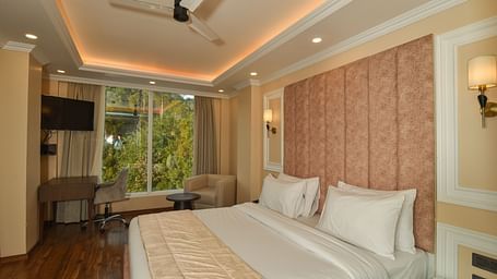  A bright and spacious hotel bedroom with a large bed, soft lighting, and large windows offering scenic mountain views.