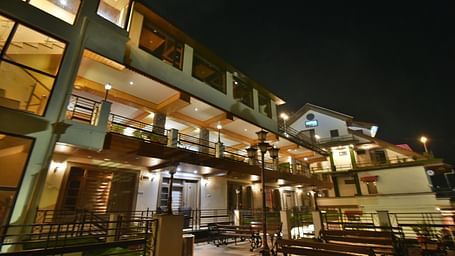 Overview of open terrace at DLS Dalhousie Valley Resort featuring benches and tables during night.