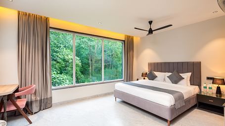 Overview of Deluxe Room at DLS Divine River Resort and  Spa featuring a  king bed , side table, chair and balcony with forest views.