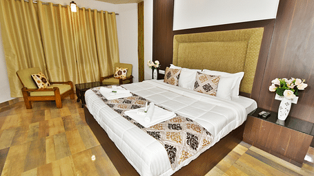 Image of the king size bed in a well furnished woodden floored room | DLS Kapoor Resort Manali
