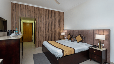 The image shows a hotel room with a large bed, two nightstands, a dresser, and a TV. There is also a door | DLS The Pearl