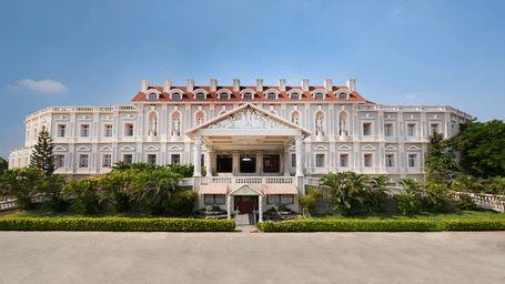 Grand white facade with red gabled roof and columned portico, framed by lush greenery - Jenneys Residency, Coimbatore